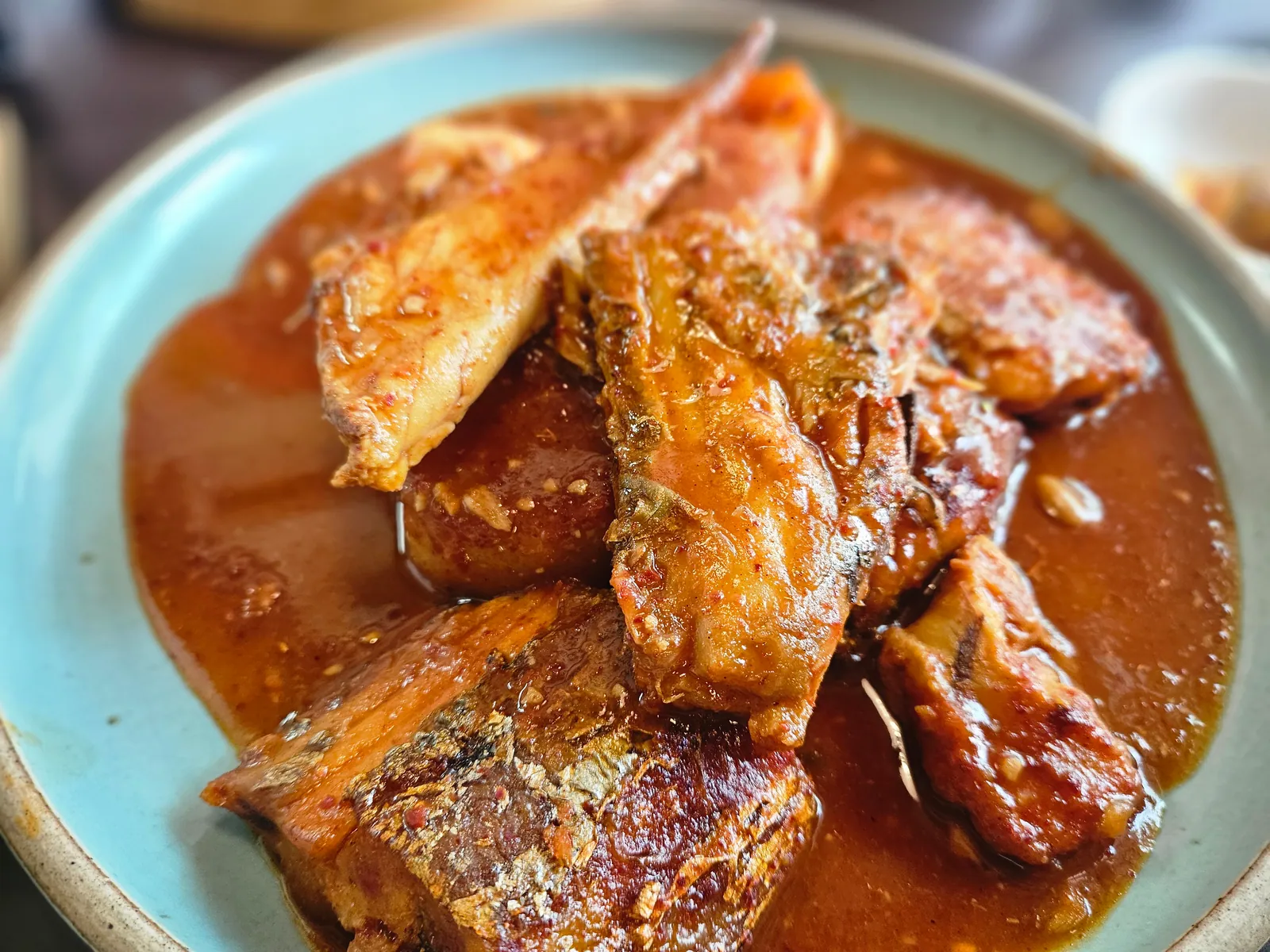 季節の魚の煮付け。赤い薬味の煮汁で煮た魚の切り身が、青緑の皿に盛られている。