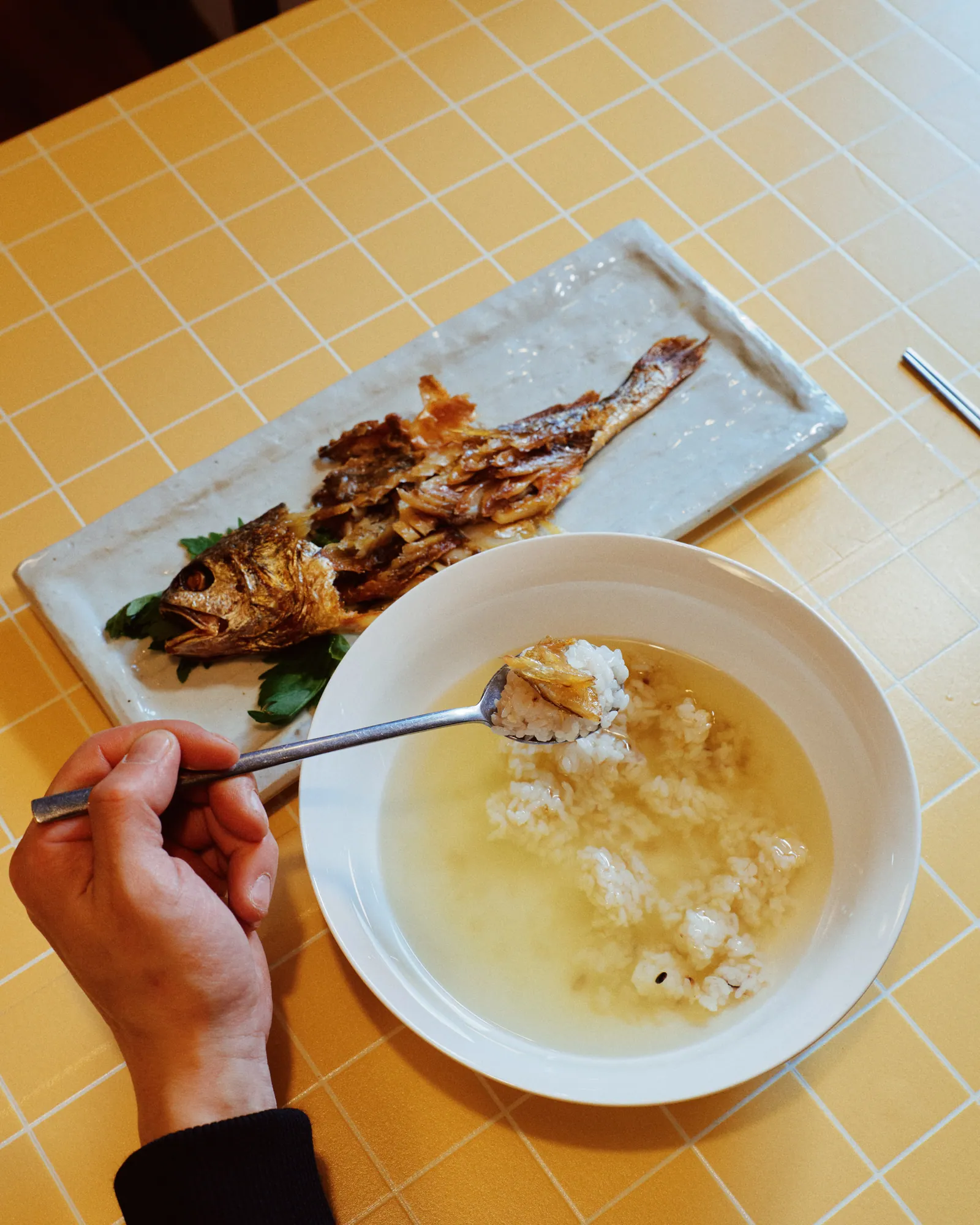ボリクルビ定食。細長い皿に焼いた干しイシモチが載り、隣の器では澄んだ汁に入れたご飯を匙ですくっている。